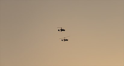 Two gyrocopters flying at sunrise, silhouettes against the morning sky, Mpumalanga, South Africa,