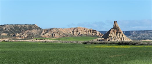 A unique rock formation rises in a green and dry landscape under a clear sky, rock formation under