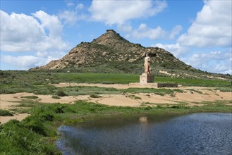 A statue stands in front of a grassy hill and a pond under a cloudy sky, Monument, Pastor