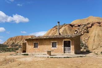 A small house stands in a dry, rocky landscape under a blue sky, Bardenas Reales Natural Park,