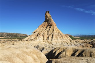 An impressive rock formation rises up in the desert-like landscape under a clear blue sky,