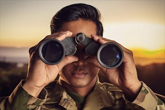 Close-up of a man in military uniform looking through binoculars into a tranquil evening landscape,