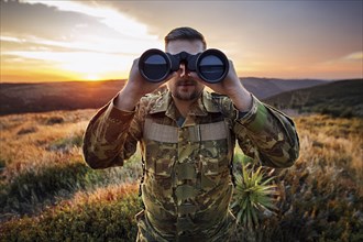 Man in camouflage clothing looks with binoculars over a green landscape at sunset, AI generated, AI