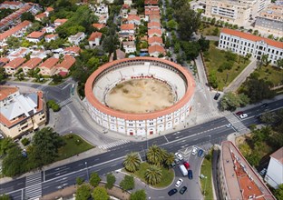 Aerial view of a historic bullring with red roofs, embedded in a town, surrounded by streets,