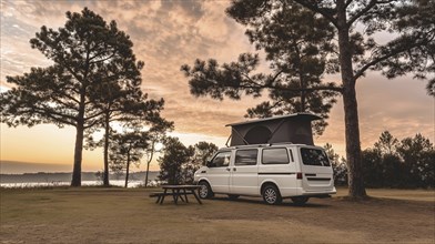 White camper van parked by trees near lake at sunset creating a tranquil outdoor camping scene, AI