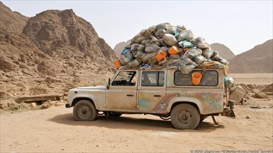 An off-road Land Rover, loaded with bags and buckets, parked in a rugged desert landscape with