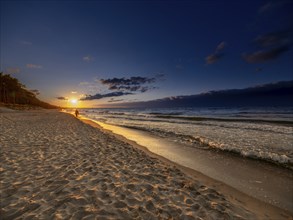 A man walks at sunset on the sandy beach on the island of Usedom on the Baltic Sea, Zempin,