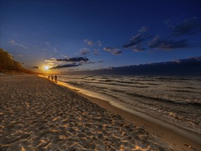 A couple holding hands at sunset on the sandy beach on the island of Usedom on the Baltic Sea,