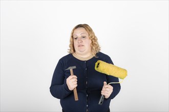 Woman looking confused at a paint roller and hammer