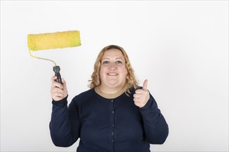 Smiling woman holding a paint roller and giving thumbs up