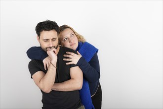 Woman hugging her partner from behind. Both with a lost look and a thoughtful expression