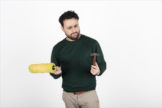 Man looking confused at a paint roller and hammer