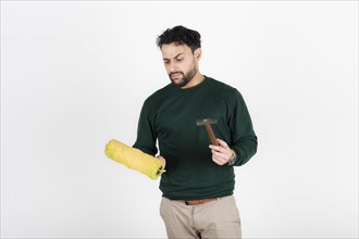 Man looking confused at a paint roller and hammer