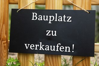 Sign with the inscription BAUPLATZ ZU VERKAUFEN on a wooden fence (symbolic image)