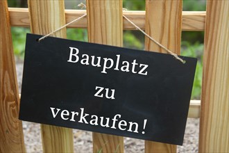 Sign with the inscription BAUPLATZ ZU VERKAUFEN on a wooden fence (symbolic image)