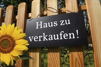 Sign with the inscription HAUS ZU VERKAUFEN on a wooden fence (symbolic image)