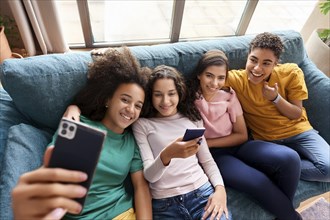 Four friends sit on a couch and take a selfie with a smartphone in a relaxed atmosphere, ai