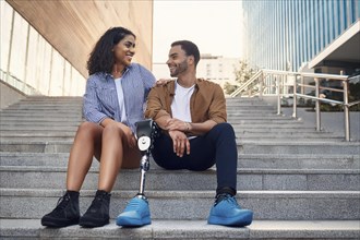 Couple, man with prosthetic leg, sitting on the steps in the city, the woman laughs at her partner