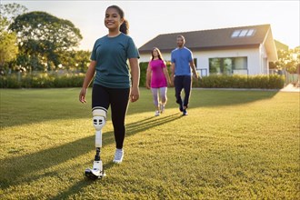 Young woman with prosthetic leg walking on the lawn, parents following her, house in the