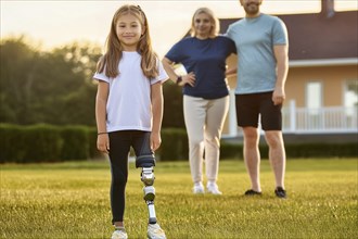 A girl with a prosthetic leg stands in the foreground while her parents watch her in the garden, ai