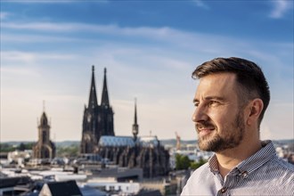 A man stands in front of a cityscape looking into the distance, with a cathedral in the background,