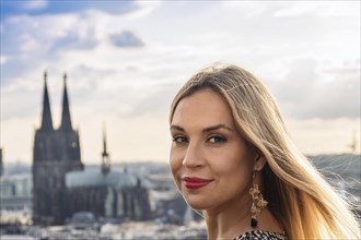 A woman stands in front of a city view with Cologne in the background and smiles, ai generated, KI