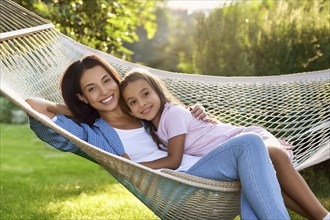 A woman and a child embrace and lie together in a hammock, smiling as they enjoy leisure time in