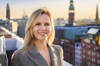 Blonde woman on a roof terrace smiling with a city view in the background, ai generated, KI