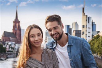 A smiling couple in front of a city skyline with modern buildings and a church tower in the