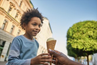 Boy with afro hair happily accepts an ice cream cone from a hand, ai generated, AI generated