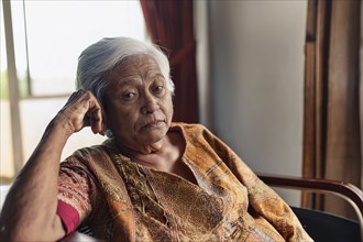 Dementia, Elderly woman in traditional dress sits thoughtfully in a room in daylight, ai generated,