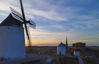 Windmills at sunset next to a castle silhouetted against a colourful sky. Atmosphere of