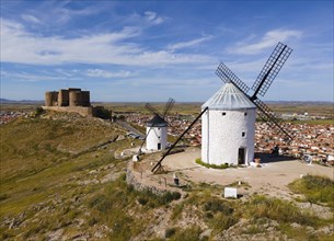 Windmills on a hill with a medieval castle in the background towering over a nearby village with a