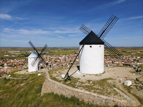 Two large white windmills overlook a small village in a wide open landscape under a clear blue sky,