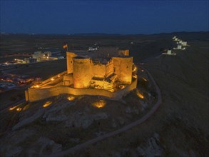 An illuminated castle at night with a dark sky and a path surrounding the castle, aerial view,