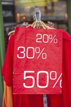 Red sign discount on a shopping bag in front of a clothing rack with t-shirts and shop window,