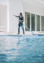 Home pool cleaning with wall brush. Male worker cleaning a home swimming pool with special brush