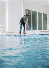 Young man cleaning a swimming pool with suction hose. Swimming pool cleaning and maintenance