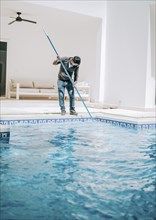 Worker cleaning a beautiful homemade swimming pool with skimmer. Maintenance person cleaning a