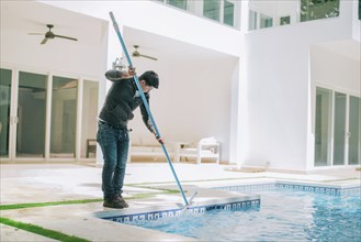 Person cleaning swimming pool with special brush. Maintenance person cleaning home pool with broom