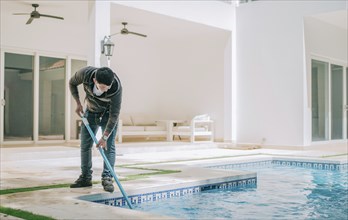 Worker cleaning a home pool with a vacuum hose. Man cleaning swimming pool with a suction hose