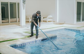 Man cleaning swimming pool with a suction hose. Worker cleaning a home pool with a vacuum hose