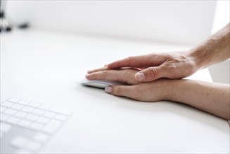 Topic: sexual assault in the workplace. A man's hand rests on a woman's hand at a desk. Berlin, 25