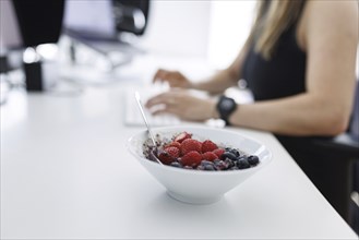 Topic: Food at the workplace. A bowl of muesli with fruit on a desk in Berlin, 25.07.2024