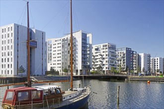 Modern buildings and houses at the harbour with boats in the water under a blue sky, renovated