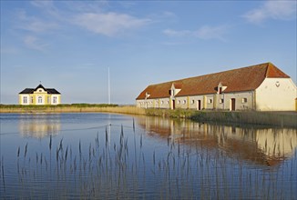 Building and house by the lake with reflection in the calm water under a blue sky, Valdemars Slot,