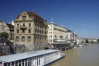 Elegant riverside buildings with small cruise ships under a bright blue sky, Rhine, Basel,