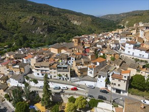 View of a village with many houses and a street with parked cars in a hilly landscape, aerial view,