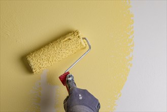 Wall is painted with yellow paint, hand with paint roller