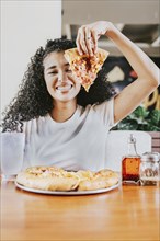 Smiling afro woman enjoying a pizza in a restaurant. Happy afro hair woman showing slice of pizza